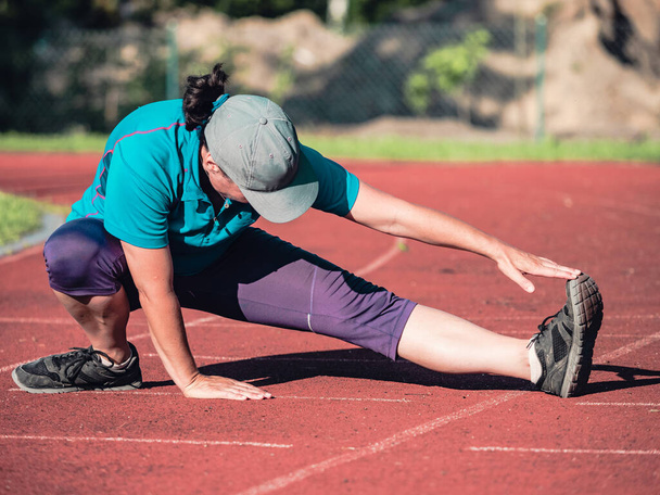 Atletik orta yaşlı kadın antrenmandan önce kırmızı koşu pistinde geriniyor, sağlıklı yaşam tarzı  - Fotoğraf, Görsel