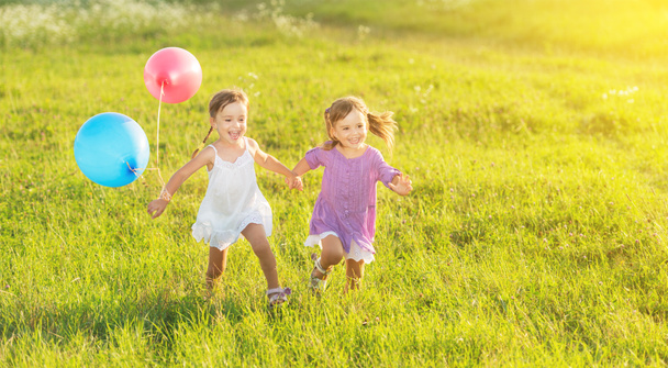 щасливі сестри-близнюки бігають навколо сміху і грають з повітряними кулями влітку
 - Фото, зображення