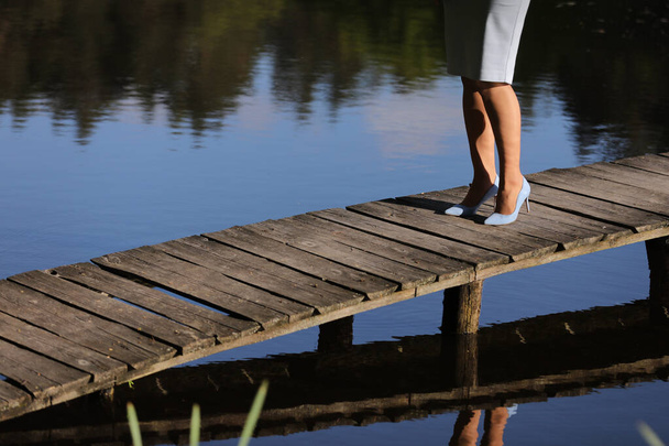 bijgesneden foto van vrouwelijke benen lopen op een houten pier op de rivier. - Foto, afbeelding
