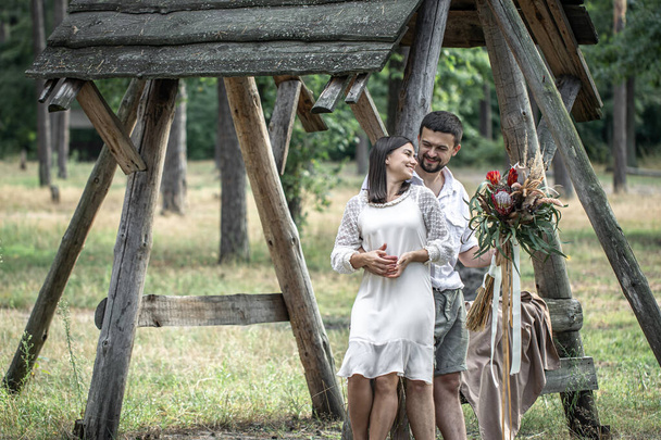 Jeune homme et femme habillés intelligemment câlins dans la forêt avec un bouquet de fleurs exotiques, romance dans le mariage. - Photo, image
