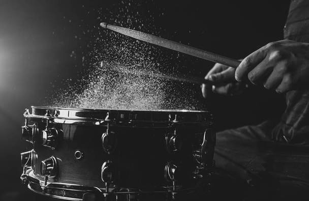 Drum Sticks schlagen Snare Drum mit plätscherndem Wasser auf schwarzem Hintergrund unter Bühnenbeleuchtung. - Foto, Bild