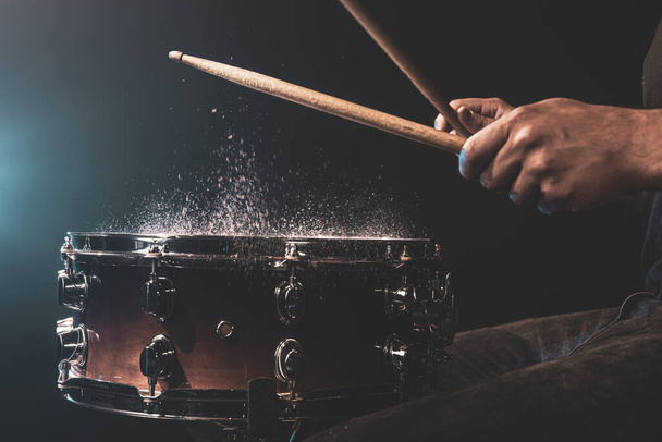 Schlagzeuger mit Schlagzeug-Sticks schlägt Snare Drum mit Spritzwasser auf schwarzem Hintergrund unter Studiolicht Nahaufnahme. - Foto, Bild