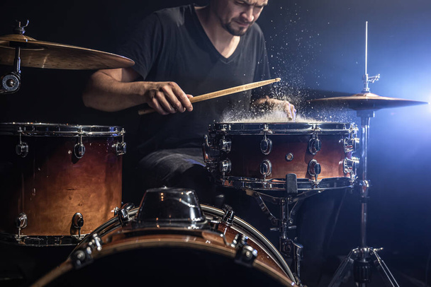 A male drummer plays drum sticks on a snare drum with splashing water in a dark room. - Photo, Image