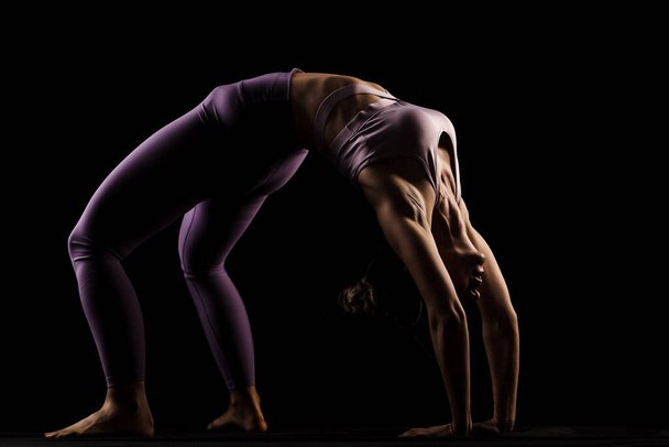 Fit girl practicing yoga in a studio. Half silhouette side lit fitness model - Photo, image