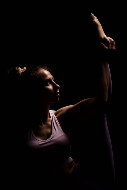 Fit girl practicing yoga in a studio. Half silhouette side lit fitness model - Foto, imagen