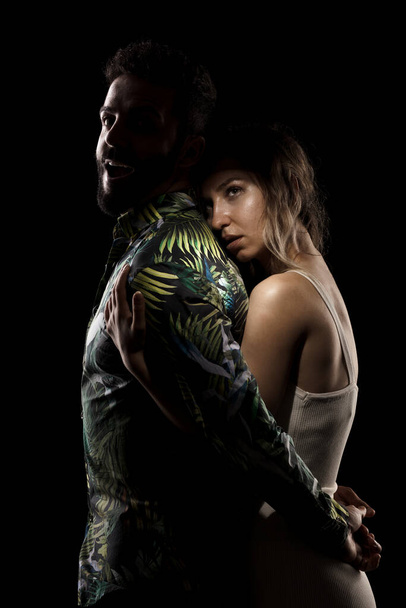 Couple posing on black background. Girl hugging boy in shadow from behind - Fotografie, Obrázek
