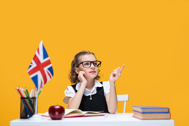 Thoughtful caucasian schoolgirl sitting at the desk with books. English lesson Great Britain flag - Foto, Imagem