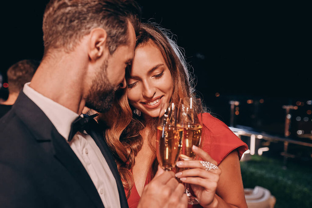 Beautiful young couple in formalwear toasting with champagne and smiling - Photo, image