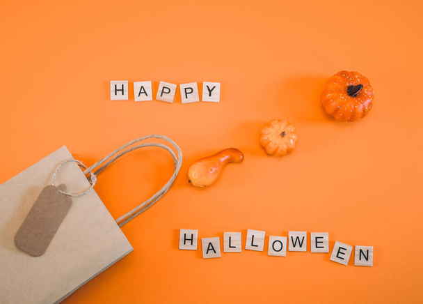 One craft bag in which decorative pumpkins are scattered diagonally and wooden cubes with the inscription: happy halloween lie on an orange background, close-up. Concept greeting card. - Fotoğraf, Görsel