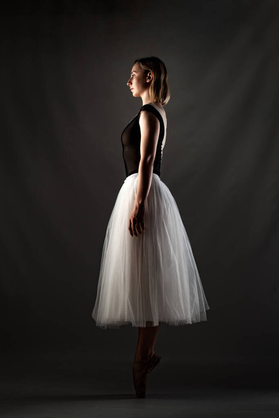 балерина з білою сукнею і чорним зверху позує на сірому фоні
 - Фото, зображення