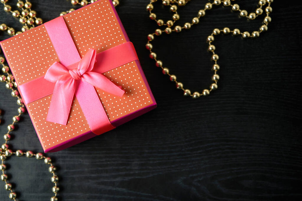 Closeup of red present box with pink ribbon and bow on the black wood - Foto, Bild
