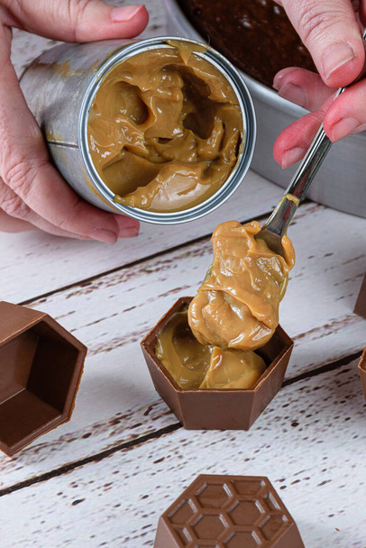 Confectioner putting a spoon of dulce de leche in small chocolate molds to make Brazilian honey cake. - Photo, Image