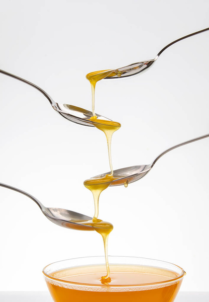 Fresh flower honey drips from a spoon into a spoon on a white background. Organic vitamin food. - Foto, immagini