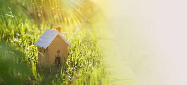 House wood model with copy space of home and life concept. Model home on green grass with sunlight abstract background. Banner size Photo - Photo, Image