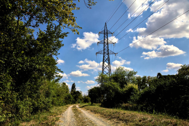 Caminho de terra delimitado por uma corrente de água com um pilão eléctrico na zona rural italiana - Foto, Imagem