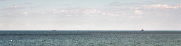 A barge carrying an construction equipment and excavator with piles of stone on either side  floats across the water of Lake Michigan at the horizon being pulled by a tug boat far in the distance. - Fotó, kép