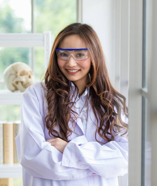 Content Asian female in white medical robe and protective glasses standing in lab and looking at camera - Foto, Bild