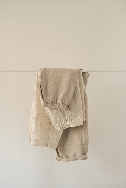 Women's aesthetic minimal fashion pastel clothes made of washed linen. Stylish female pants and trousers on hanger on white background. Fashion blog, website, social media - 写真・画像