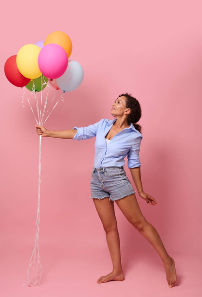 Full length body size view of gorgeous stunning cheerful glad wavy-haired mixed race African lady holding in hand bunch air balls corporate event organization delivery isolated pink color background - 写真・画像