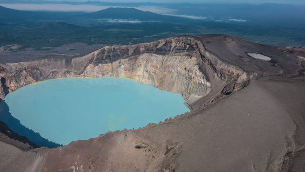 Turquoise acidic lifeless lake in the crater of a volcano. Deposits of sulfur on the surface. On the steep rocky slopes, devoid of vegetation, the shadow of a helicopter. Aerial view. Kamchatka - Photo, Image