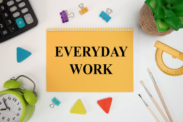 Everyday Work is written in a notebook on an office table with office supplies. - Zdjęcie, obraz
