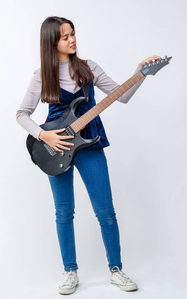 Portret uroczej, uśmiechniętej nastolatki z Tajlandii i Turcji trzymającej i grającej na gitarze elektrycznej. Junior mieszane wyścigu gitarzysta gra na instrumencie patrząc na aparat odizolowany w białym tle - Zdjęcie, obraz