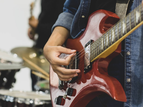 Close-up shot of young female musician hands playing the electric guitar. Selective focus on the guitarist's hands with a drum in the background. Guitarist playing music together with classmate - Foto, Bild