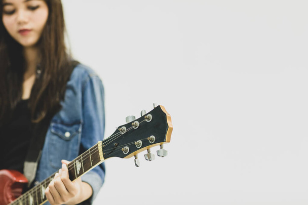 Κοντινό πλάνο μιας νεαρής κιθαρίστριας που παίζει ηλεκτρική κιθάρα. Επιλεκτική εστίαση στην ηλεκτρική κιθάρα με έναν θολή παίκτη απομονωμένο σε λευκό φόντο. Έννοια του εφηβικού τρόπου ζωής - Φωτογραφία, εικόνα