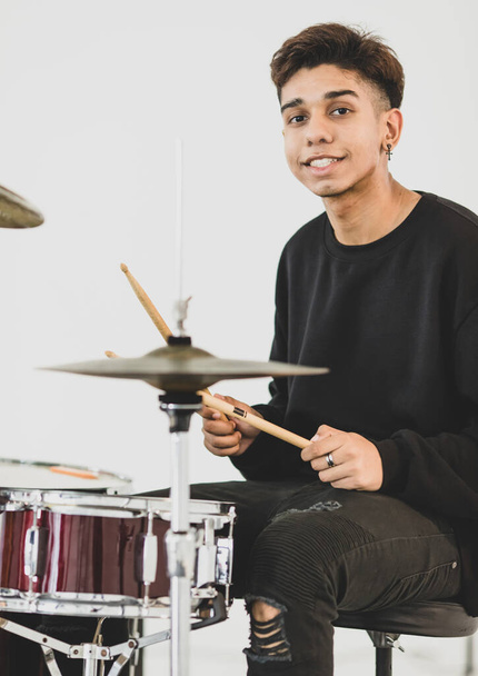Front view portrait shot of teenage drummer playing the music. Young musician playing the drum while looking at the camera and smiling. Junior student playing an instrument with white background - Photo, Image