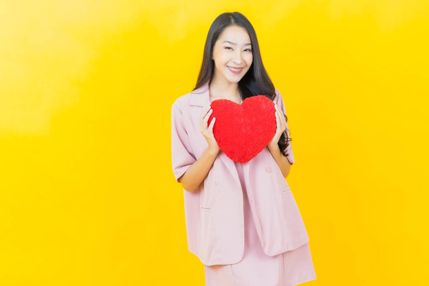 Portrait beautiful young asian woman smile with heart pillow shape on color background - Photo, Image
