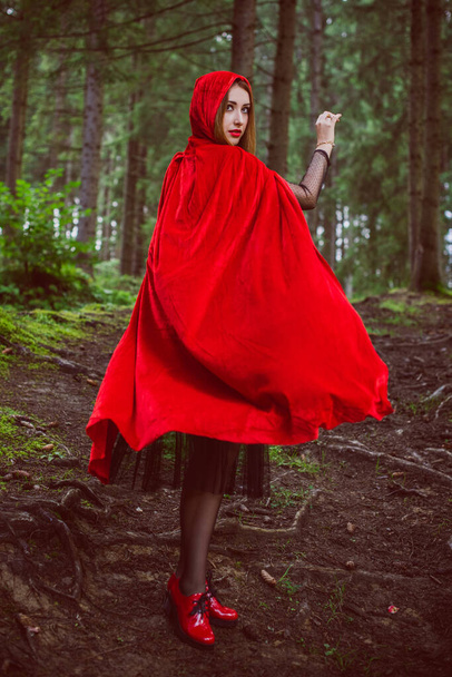 Het concept van Halloween. Mooi en eenvoudig kostuum van kleine rode kap. Een mysterieuze figuur met kapuchon in mistig bos. Meisje met een rode regenjas. Cosplay sprookje klein rood paardrijden kap - Foto, afbeelding