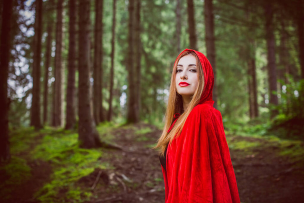 Konzept von Halloween. Schönes und einfaches Kostüm aus roter Kapuze. Geheimnisvolle Kapuzenfigur im nebligen Wald. Mädchen im roten Regenmantel. Cosplay Märchen Rotkäppchen - Foto, Bild