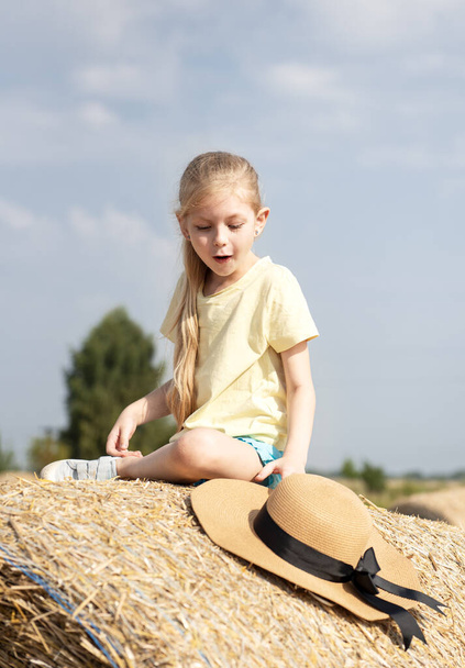 Egy kislány szórakozik a búzamezőn egy nyári napon. Gyermek játszik szénabála mező a betakarítási idő alatt. - Fotó, kép