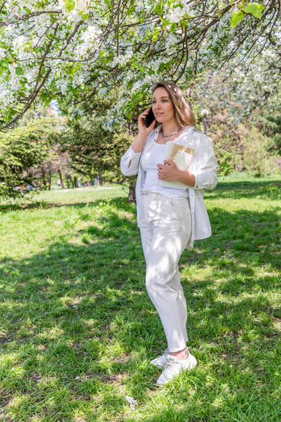 Young business woman talking on phone while standing in city park. Walk during lunch break. Concept permanent use of the gadget. - Foto, imagen
