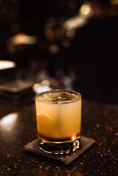 Klasszikus savanyú koktélt jéggel, egy régimódi pohárban, narancssárgával a bárban. - Fotó, kép