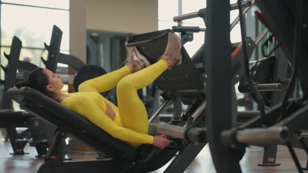 Hispánská žena pomocí tiskového stroje ve fitness klubu. Mladá žena cvičí na nohou v simulátoru ve žlutém sportovním oblečení, - Záběry, video