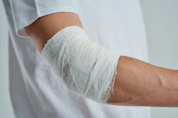 male patient in a white T-shirt with a bandaged hand isolated background - Photo, Image