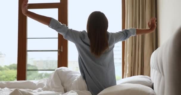 Glückliche junge Dame sitzt morgens im Bett und streckt die Arme aus - Filmmaterial, Video