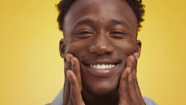 真の幸せ。Close up portrait of wide smiling african american guy massaging his cheeks with smiley face - 映像、動画