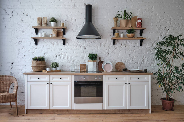 μοντέρνο φωτεινό εσωτερικό κουζίνας με λευκούς τοίχους, έπιπλα, σκεύη, ράφια - Φωτογραφία, εικόνα