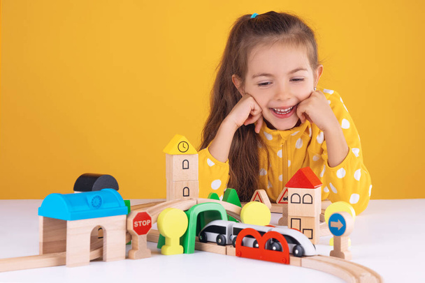 Cute kid, little girl playing with wooden toys train and railway road - Photo, Image