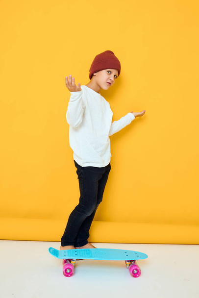 Cheerful little kid in a white sweater skateboard entertainment isolated background - Zdjęcie, obraz