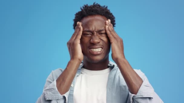 Schrecklicher Migräneanfall. Junger emotionaler afrikanisch-amerikanischer Mann massiert seine Schläfen und leidet unter akuten Kopfschmerzen - Filmmaterial, Video