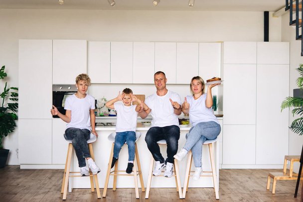 Fröhliche Familie zu Hause. Mama, Papa und zwei Söhne. Sie sitzen in der Küche auf Stühlen. Freude und Jubel. - Foto, Bild