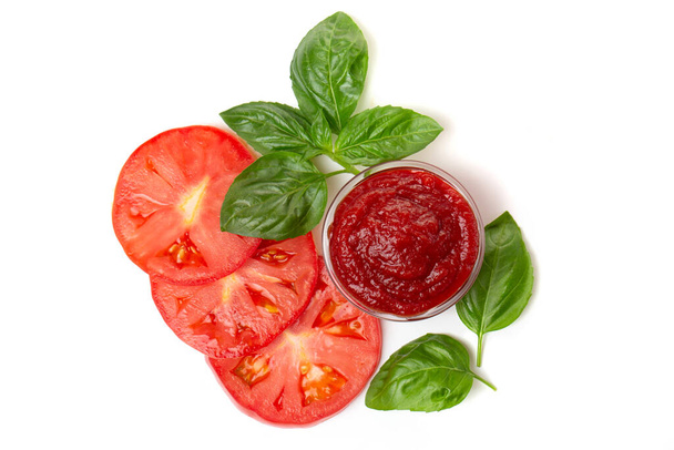 Ketchup (tomato paste) in a saucepan with basil leaves and tomato slices on a white background. - Foto, Imagen