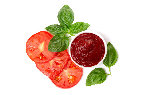 Ketchup (tomato paste) in a saucepan with basil leaves and tomato slices on a white background. - Foto, Imagem