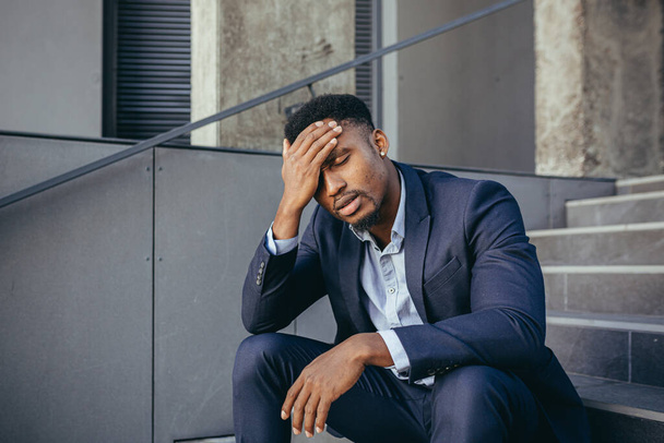Afrikaans zakenman zit gefrustreerd op de trap depressief door de resultaten van zijn werk, hand in hand achter zijn hoofd - Foto, afbeelding