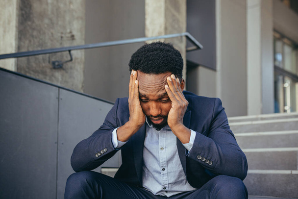 african businessman sitting frustrated on the stairs depressed by the results of his work, holding hands behind his head - Fotó, kép