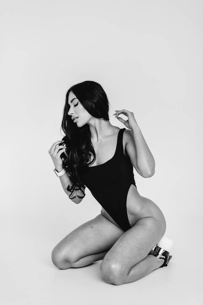 Young sexy brunette in a black bodysuit on a white background. The perfect athletic figure. - Фото, изображение