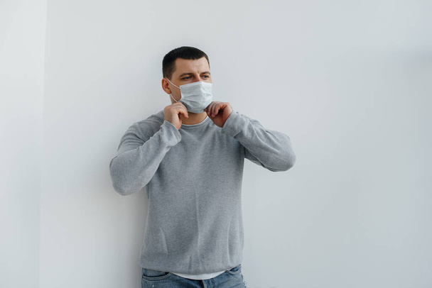 A young man stands on a gray background wearing a mask during a quarantine with free space. Quarantine in the mask - Photo, Image